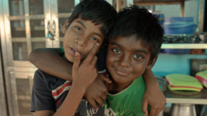 Two young Indian kids embracing while facing camera